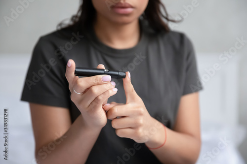 Close up view young African woman sit indoors holding portable glucose meter electronic device doing checkup test blood sugar. Patient with diabetes mellitus health problem, modern tool tech concept