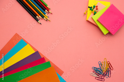 Pencils, multicolored papers and paper clips on a pink background