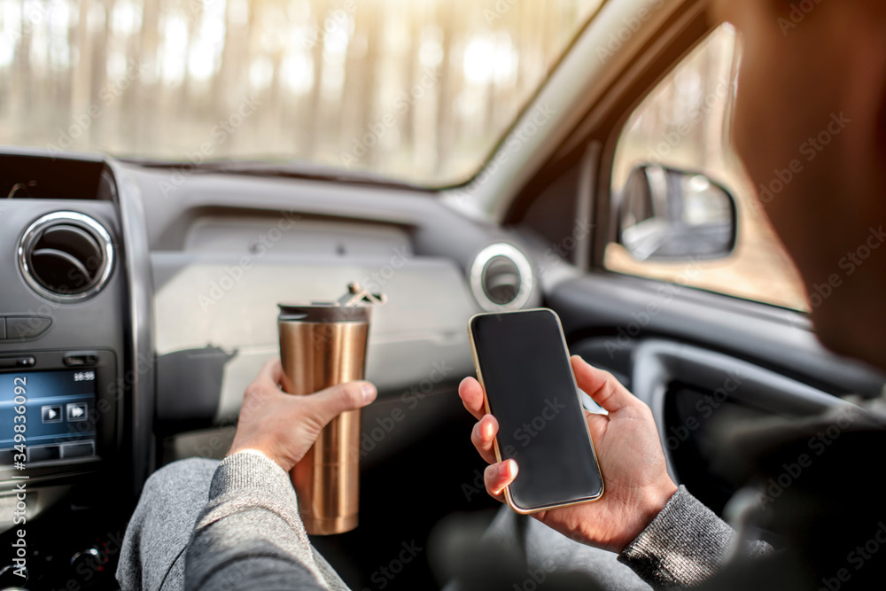 Close-up of hands and thermos with smartphone in car. Travel concept
