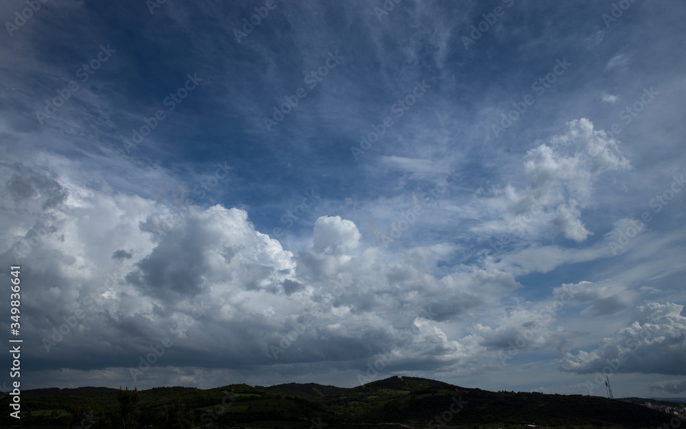 Wide angle photo of cloudy blue sky. Mountains appear under the photo. Width angle.