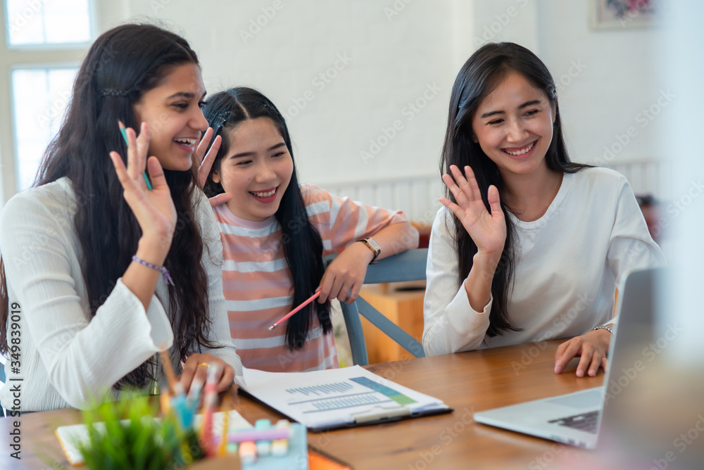 Three young female sitting at table and waving their hands while making video call with laptop. Remote working, working from home concept. Three young female sitting at table and waving their hands while making video call with laptop. Remote working, working from home concept.
