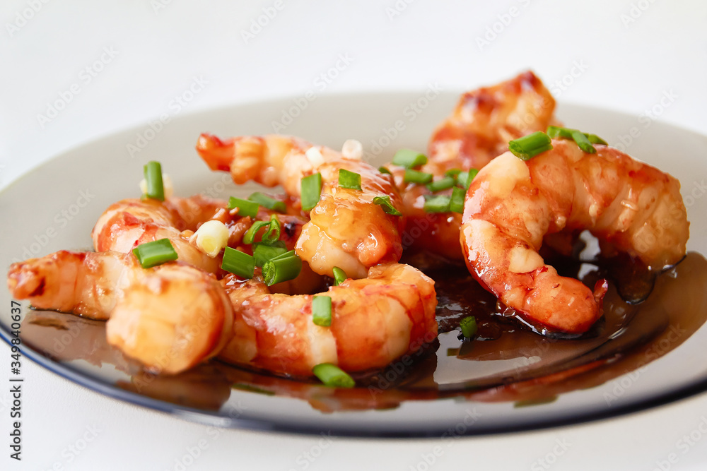 Large pacific shrimps in sweet and sour sauce with chopped green onions on a glass plate. Large pacific shrimps in sweet and sour sauce with chopped green onions on a glass plate.