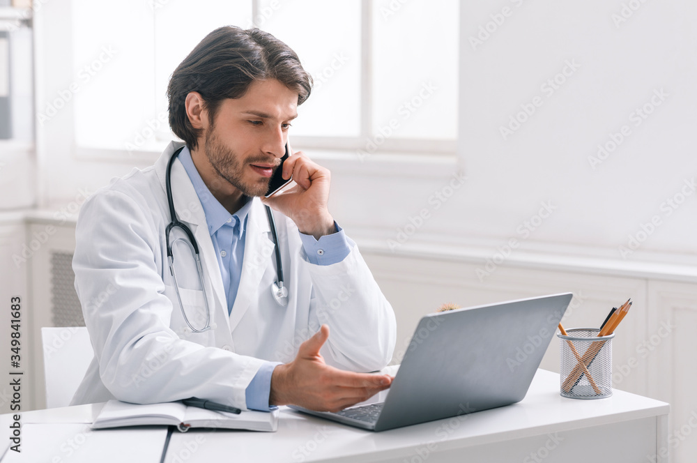 Serious doctor working on laptop and having phone call Serious doctor working on laptop and having phone call
