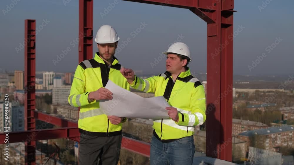 Two male builders engineers men, contractor investor worker foreman architect in hard hat discussing drawing blueprint on construction site of industrial building outdoors. city background 4 k slow-mo Two male builders engineers men, contractor investor worker foreman architect in hard hat discussing drawing blueprint on construction site of industrial building outdoors. city background 4 k slow-mo