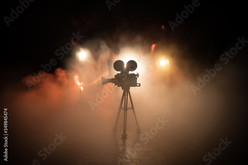 Movie concept. Miniature movie set on dark toned background with fog and empty space. Silhouette of vintage camera on tripod. photo
