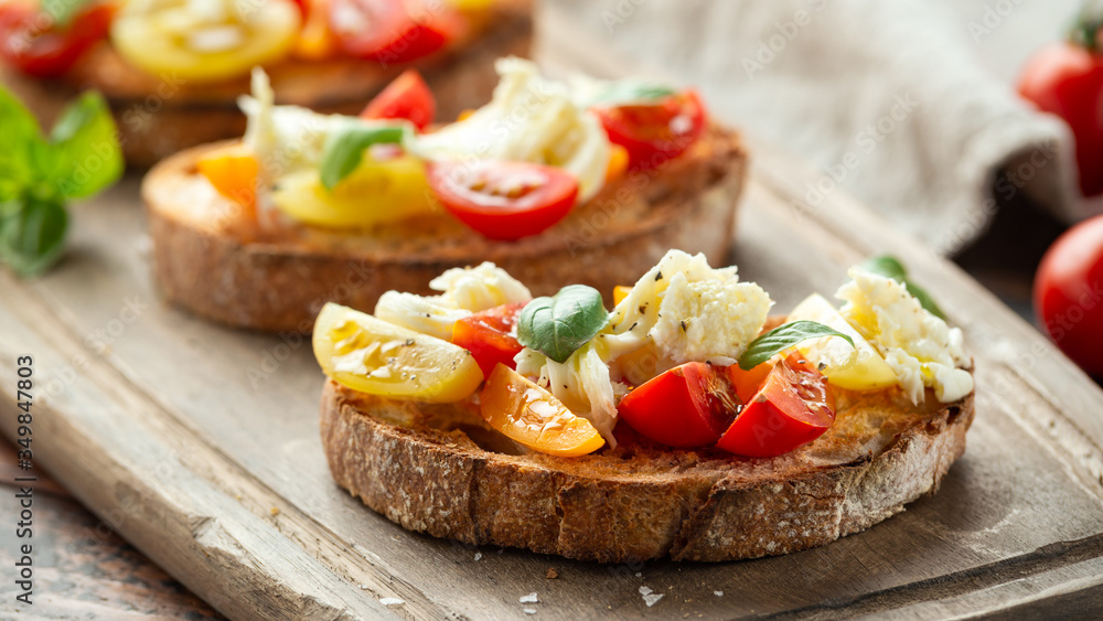 Tomato bruschetta and mozzarella cheese with basil on a rustic wooden board Tomato bruschetta and mozzarella cheese with basil on a rustic wooden board