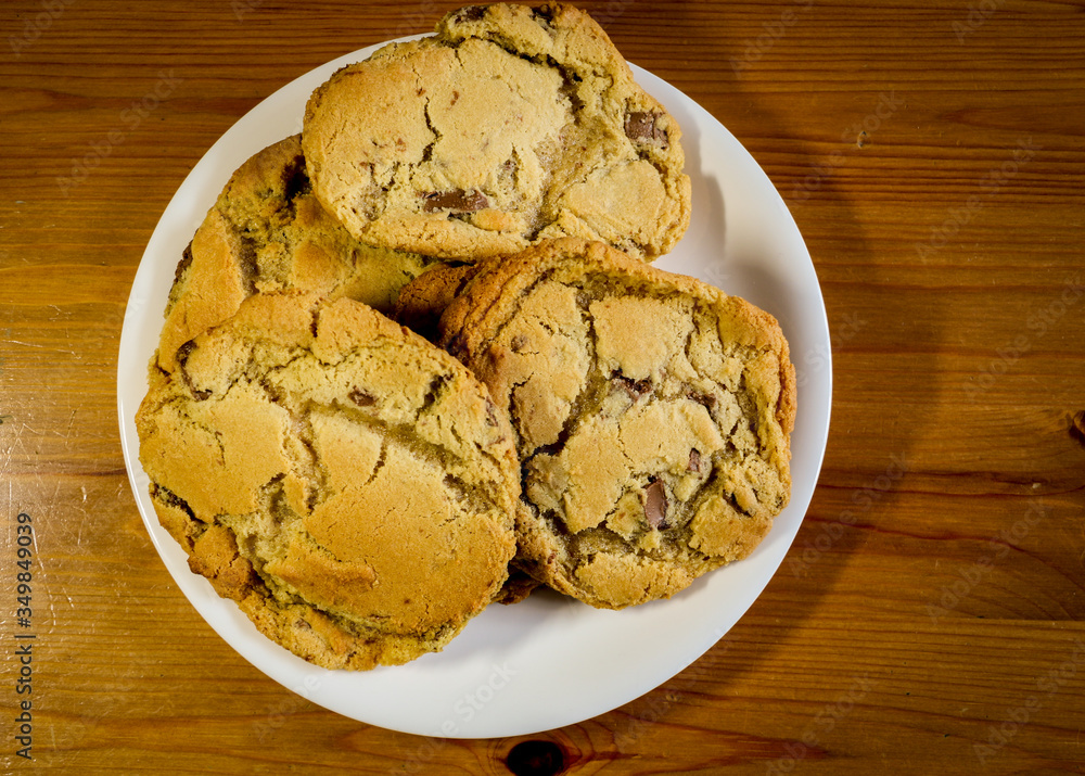 Home baking. Homemade chocolate chip cookies on a white plate and a glass of milk in a kitchen setting Home baking. Homemade chocolate chip cookies on a white plate and a glass of milk in a kitchen setting