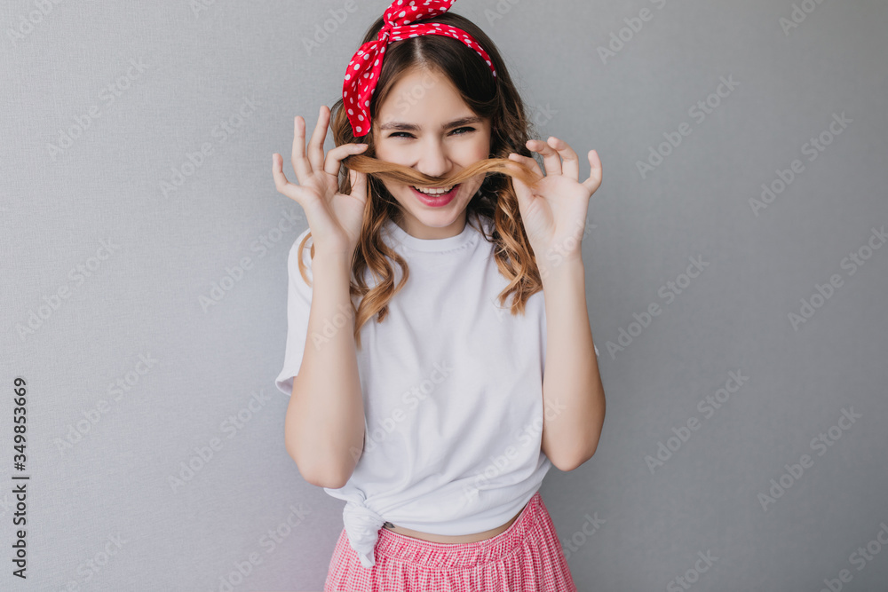 Blissful girl with wavy hairstyle making funny faces. Attractive caucasian woman playing with her curly hair on light background. Blissful girl with wavy hairstyle making funny faces. Attractive caucasian woman playing with her curly hair on light background.