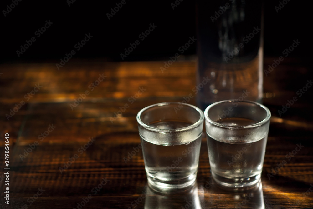 Frozen glasses with alcohol near the bottle. Drinks on a dark brown table. Transparent utensils on a black background. Old shabby boards under glass. Frozen glasses with alcohol near the bottle. Drinks on a dark brown table. Transparent utensils on a black background. Old shabby boards under glass.