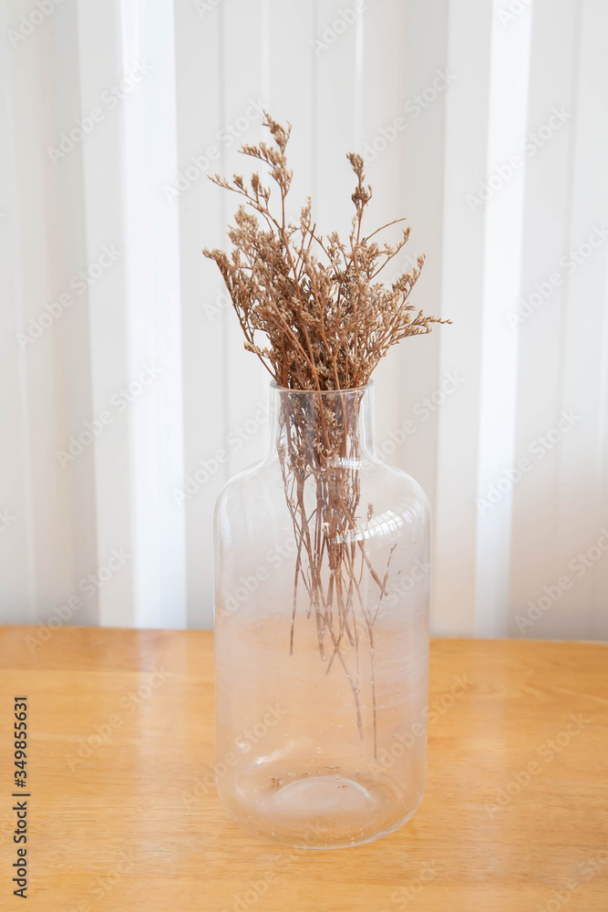 Small bouquet of dry flowers in glass vase on wooden table. Minimalism and vintage concept.