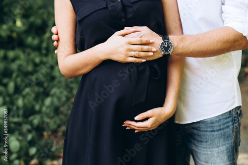 Future parents. A young pregnant woman walks in nature. Hands on the belly close-up. Waiting for a miracle. A man and a woman hold their hands in the shape of a heart.