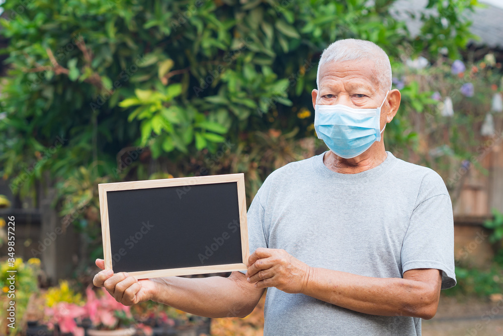 A portrait of an elderly man wearing a face mask and holding a blackboard standing in a garden. Mask for protect virus, coronavirus, pollen grains. Concept of old people and healthcare A portrait of an elderly man wearing a face mask and holding a blackboard standing in a garden. Mask for protect virus, coronavirus, pollen grains. Concept of old people and healthcare