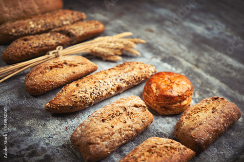 Fresh bakery food. Crusty loaves of mixed breads and buns and ears of wheat on rustic table background. Shallow DOF and copy space for your advertising text message
