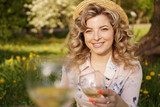 Women clinking glasses with tasty wine on light background at summer day. Happy blonde with curly hair in a straw hat