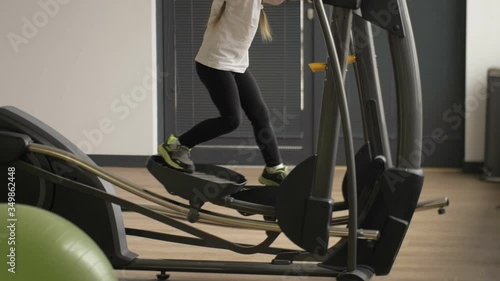 Little girl with pigtails is trying to do fitness on an adult simulator. Healthy lifestyle since childhood. photo