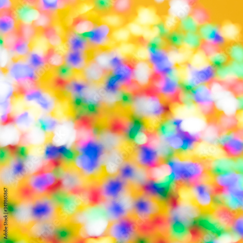 Blurred background with multicolored sparkles and lights on a yellow background