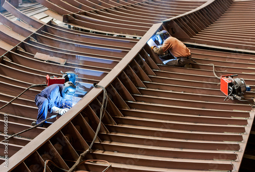 Professional shipbuilders working with a safety helmet, welding parts of a new ship's hull