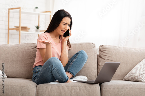 Frustrated woman talking on mobile phone sitting on sofa