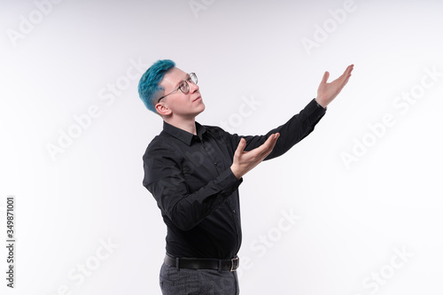 Young blue haired man is stretching his hands, excitedly showing something, studio, light background, copy space