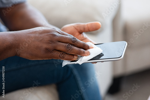 Gadget Hygiene. Unrecognizable African Man Disinfecting Smartphone Screen With Antibacterial Wipe