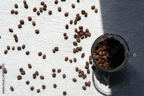 A Cup filled with coffee beans. Coffee beans are scattered on the white surface of the table