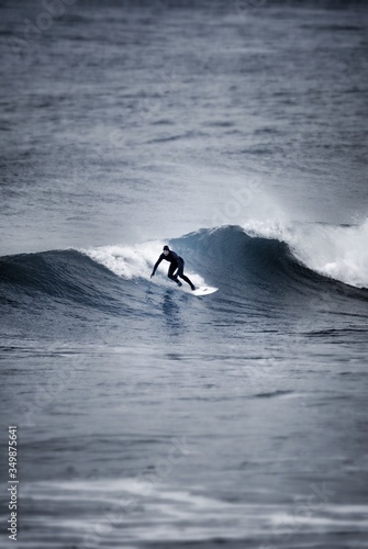 Surfer in full wetsuit and hood surfing a cold looking wave, Cornwall, UK