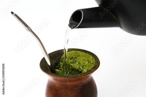 close-up de uma cuia de porongo velha com erva-mate e bomba de inox usadas, recebendo água de chaleira para o preparo do chimarrão, tradicional no sul do Brasil.