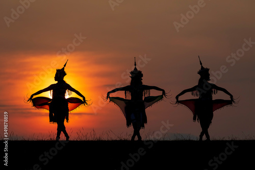 The black silhouette of three Manohra actors dancing in the park in the evening. Manohra performance is a folk dance that has a long history in southern Thailand.