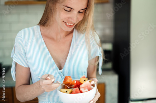 Young adult girl standing on kitchen  enjoying fruit salad
