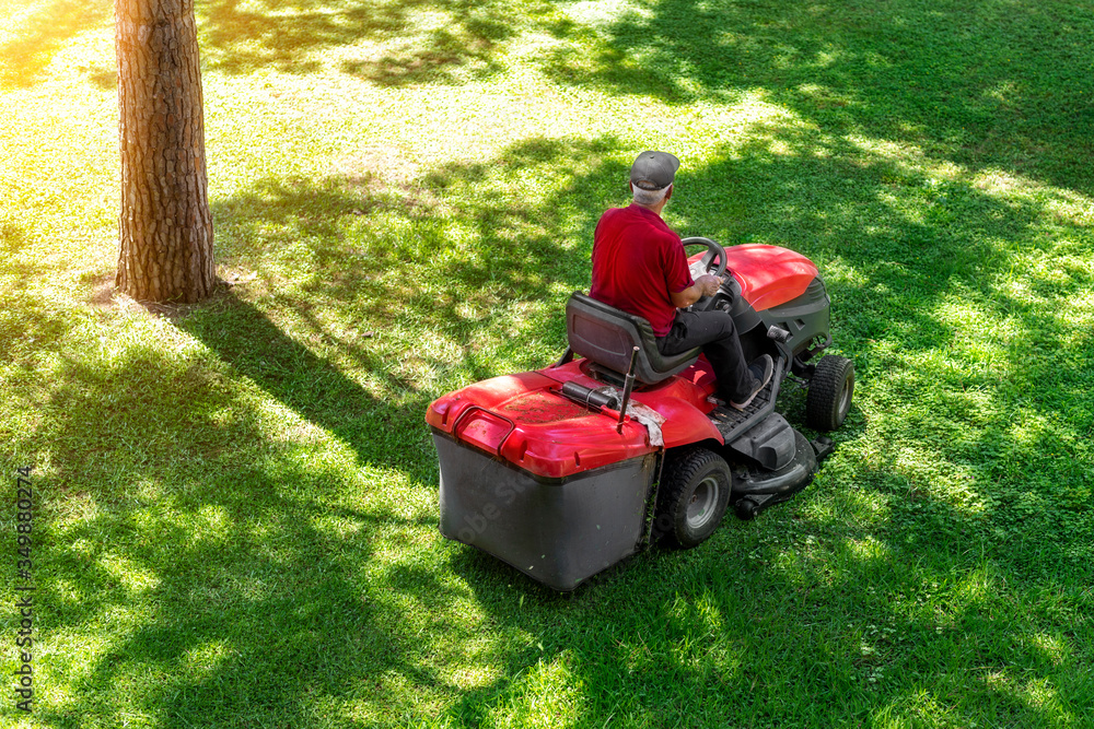 Top down above view of professional lawn mower worker cutting fresh green grass with landcaping tractor equipment machine at city park. Garden and backyard landscape lawnmower service and maintenance Top down above view of professional lawn mower worker cutting fresh green grass with landcaping tractor equipment machine at city park. Garden and backyard landscape lawnmower service and maintenance