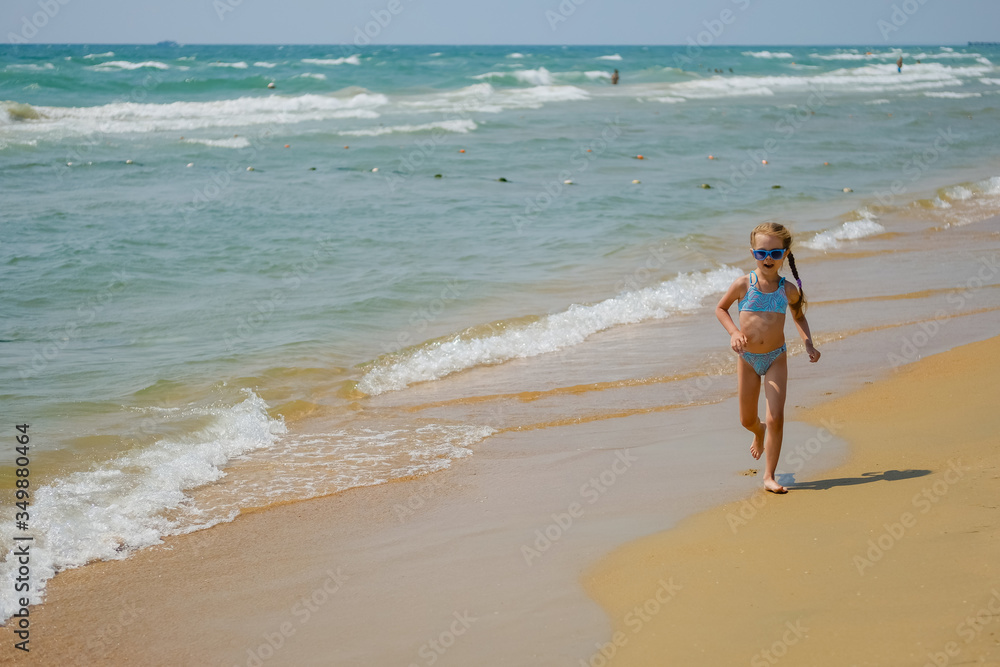 Child in sunglasses on the ocean. Little girl on the beach.