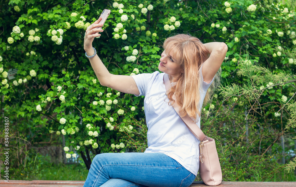 Young woman girl on a park bench uses a smartphone taking a selfie and communicating via video communication. Technology and modern lifestyle concept. A blogger makes outdoor content for his audience. Young woman girl on a park bench uses a smartphone taking a selfie and communicating via video communication. Technology and modern lifestyle concept. A blogger makes outdoor content for his audience.
