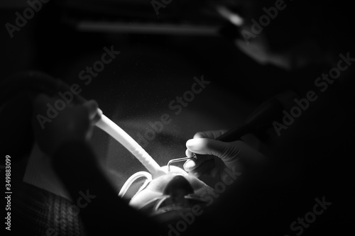 Hands of a dentist with a tool during medical procedures in the light of a spotlight.