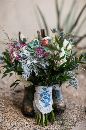 vintage wedding bouquet with blue handkerchief wrapped around stems leaning against cowboy boots