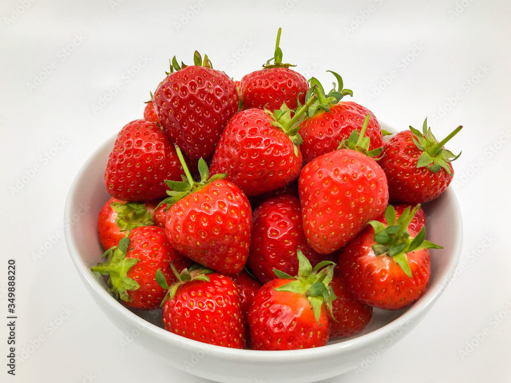 Plump ripe fresh strawberries in a white bowl on a plain white background. Plump ripe fresh strawberries in a white bowl on a plain white background.