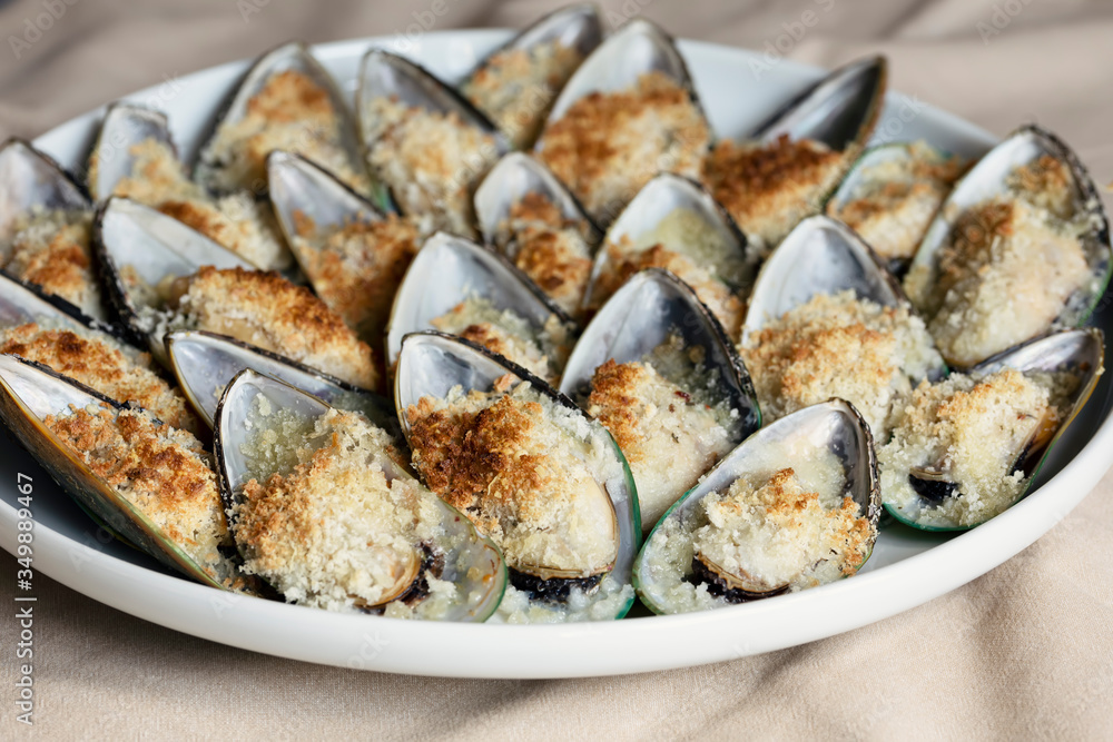 Mussels baked with parmesan, bread crumb and herb butter served on a plate. Food background. Mediterranean cuisine. Concept for a tasty and healthy meal. Close up. Mussels baked with parmesan, bread crumb and herb butter served on a plate. Food background. Mediterranean cuisine. Concept for a tasty and healthy meal. Close up.