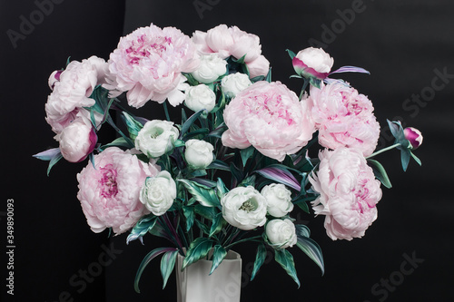 Decoration artificial peonies and white roses in vase on wood chair on black background