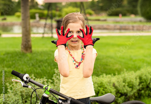a girl stands next to a Bicycle in red gloves against the background of a beautiful green Park