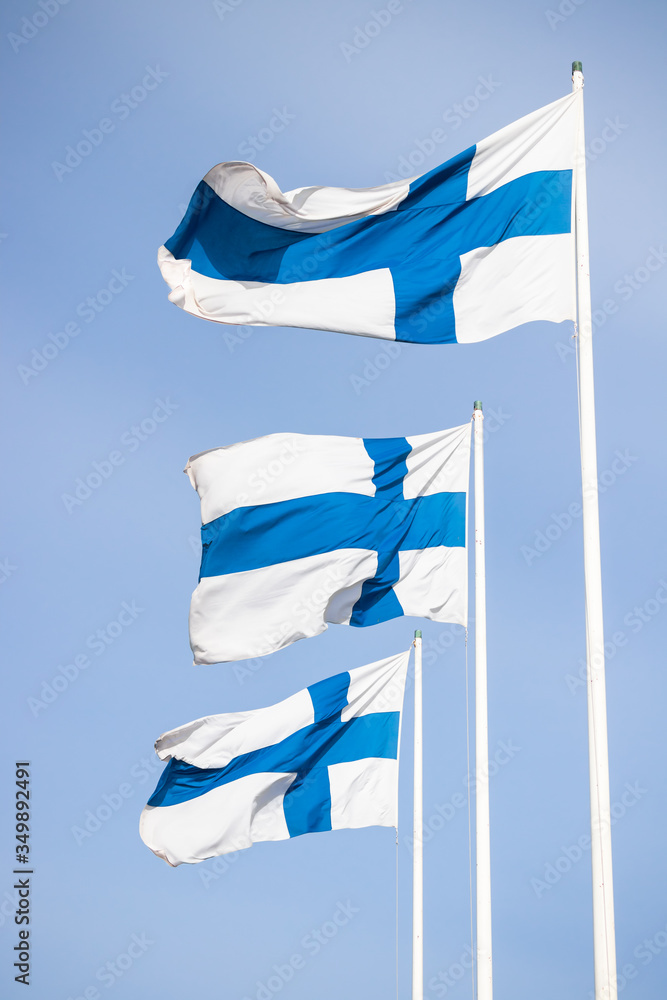 Obraz premium Three finnish national flags on the wind against the blue sky