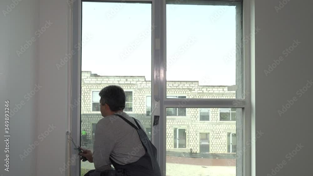 Worker take white paint from bucket with roller and paint window side Worker take white paint from bucket with roller and paint window side