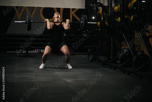 Athletic muscular man with perfect beautiful body wearing sportswear lifting heavy barbell from floor during sport workout training in modern dark gym. Concept of healthy lifestyle.