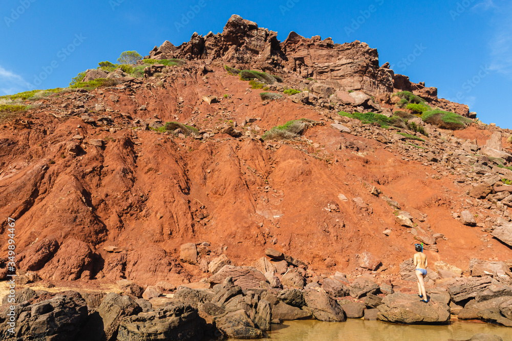 Fototapeta premium sensual unrecognizable woman in bikini looks at the mountain landscape and red sand on the beach el pilar in menorca (balearic islands, spain)