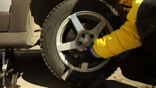 Woman changes car wheel: unscrewing by wrench front view
