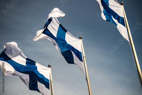 Three finnish national flags on the wind against the blue sky