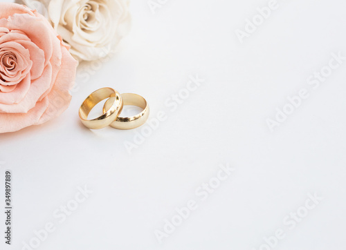 Golden wedding rings and two roses in soft tones on white background