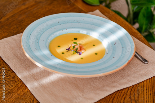 cream of salmon soup, in a bright blue plate, decorated with pieces of salmon, microgreens and butter. On the background of a wooden table.