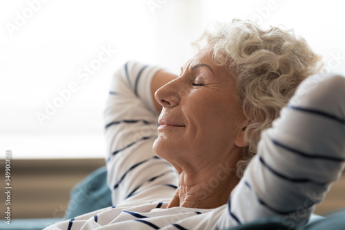 Photography Side close up head shot view tranquil calm middle aged hoary woman crossed hands behind head, relaxing on cozy sofa alone