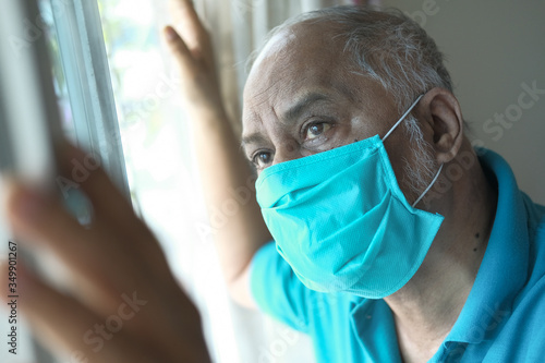 senior man with face mask looking through window 
