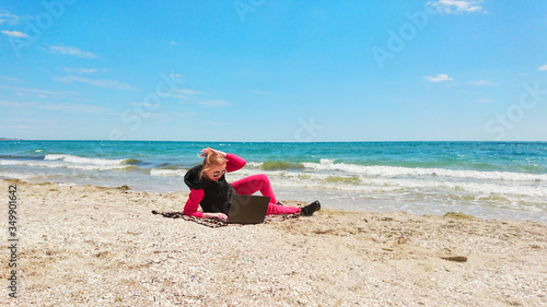 Girl on the seashore with a laptop. Rest, happiness, nature, distant work.