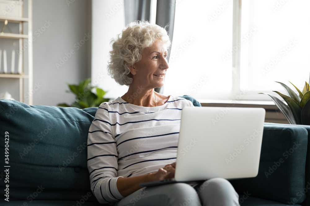 Distracted from computer work middle aged smiling woman lost in thoughts, looking away at window. Dreamy senior mature granny planning vacation time, resting with laptop on comfortable sofa at home. Distracted from computer work middle aged smiling woman lost in thoughts, looking away at window. Dreamy senior mature granny planning vacation time, resting with laptop on comfortable sofa at home.
